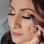 Woman receiving glamorous makeup with glitter eyeshadow and long lashes.